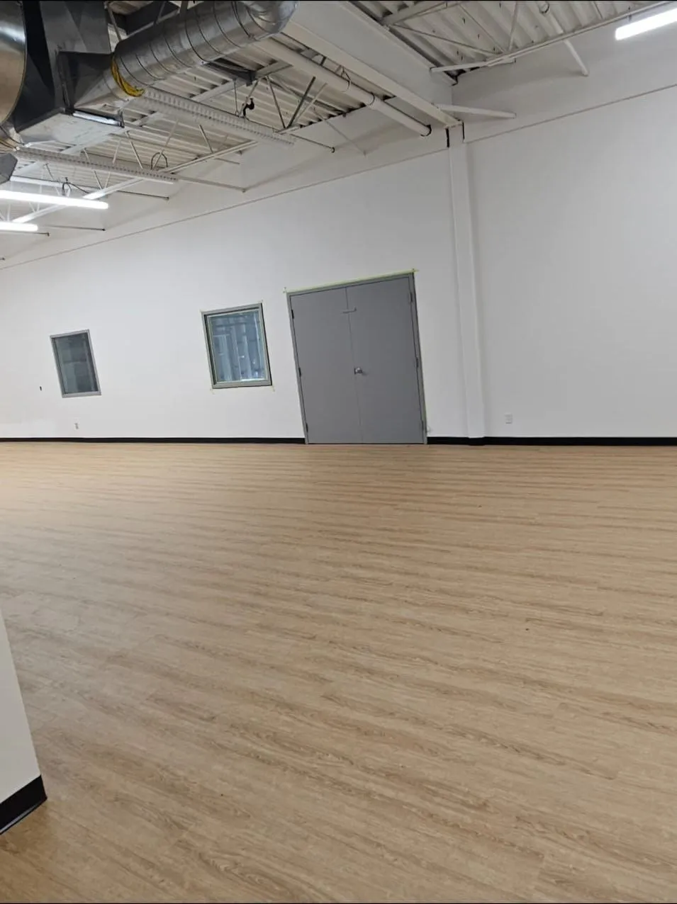 Finished open industrial-flex room with new wood-look LVP, white walls, and new duct and lighting on the exposed ceiling