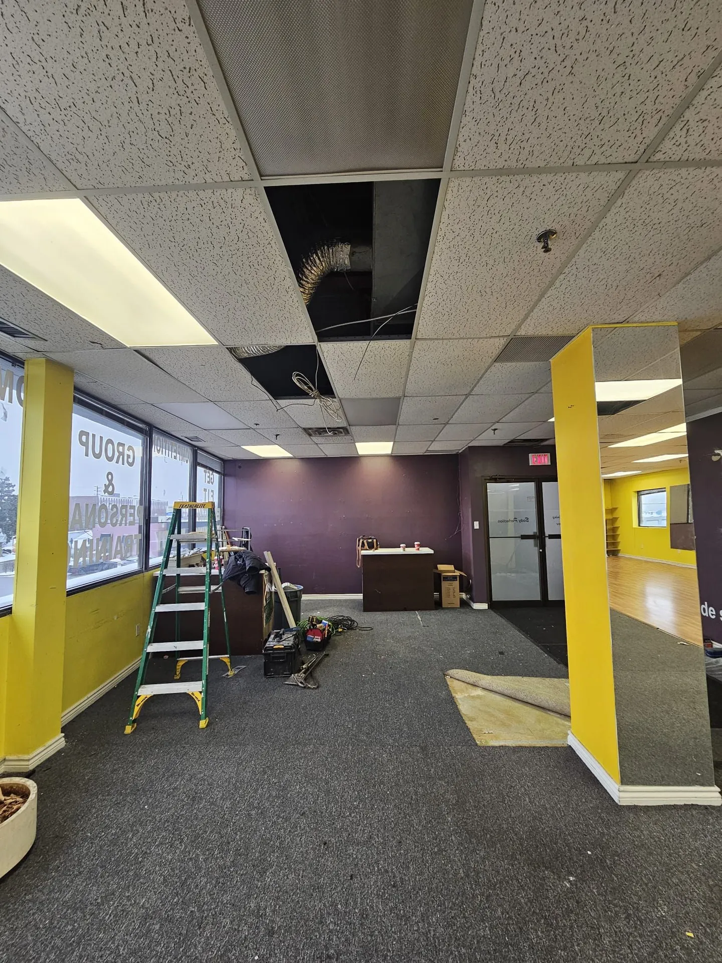 Old tenant fitness studio at demolition start with damaged drop ceiling and ladder